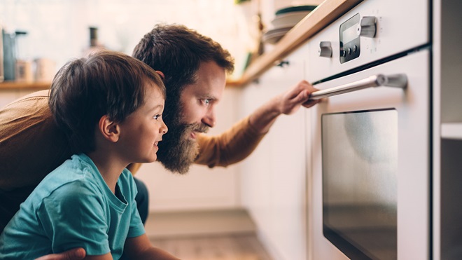 father and son looking at food cooking in oven